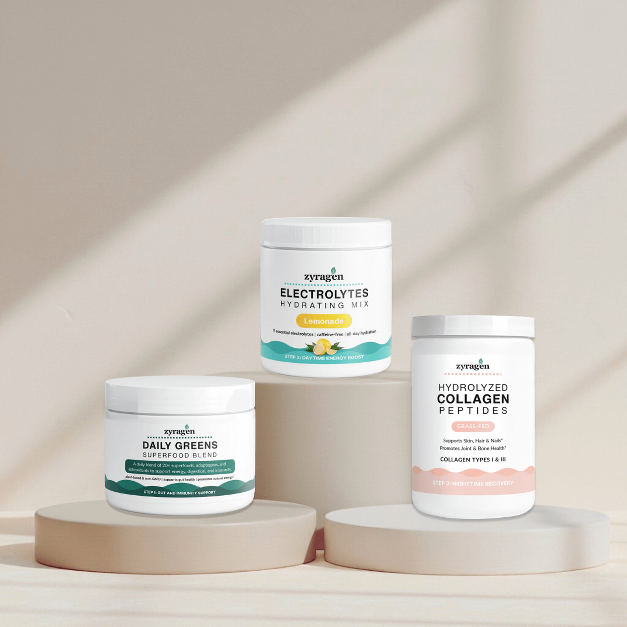 Zyragen The Daily Ritual supplement containers on a neutral background. A tub of Daily Greens, a tub of Electrolytes in Lemonade flavor and a tub of Collagen.